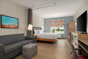 Habitación de hotel con cama, sofá, televisión, escritorio y ventana con vistas.