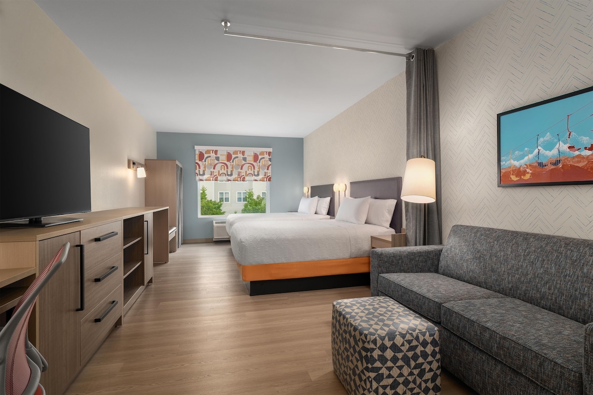 Une chambre d’hôtel moderne avec un lit, un canapé, une télévision et un tableau au mur.