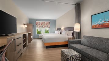 A modern hotel room with a bed, a sofa, a TV, and a painting on the wall.