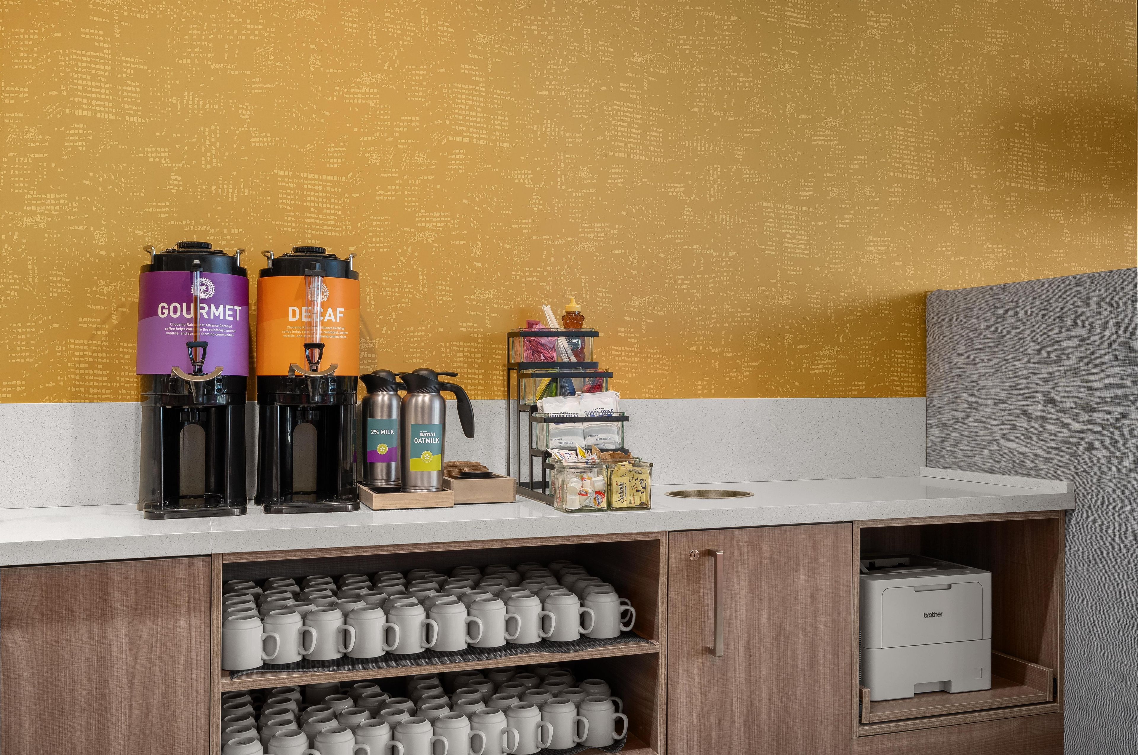 A coffee station with two coffee makers, a honey jar, and a coffee machine on a counter.