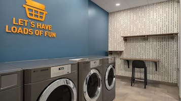 A laundry facility with commercial dryers and a wall sign that reads 'LET'S HAVE LOADS OF FUN'.