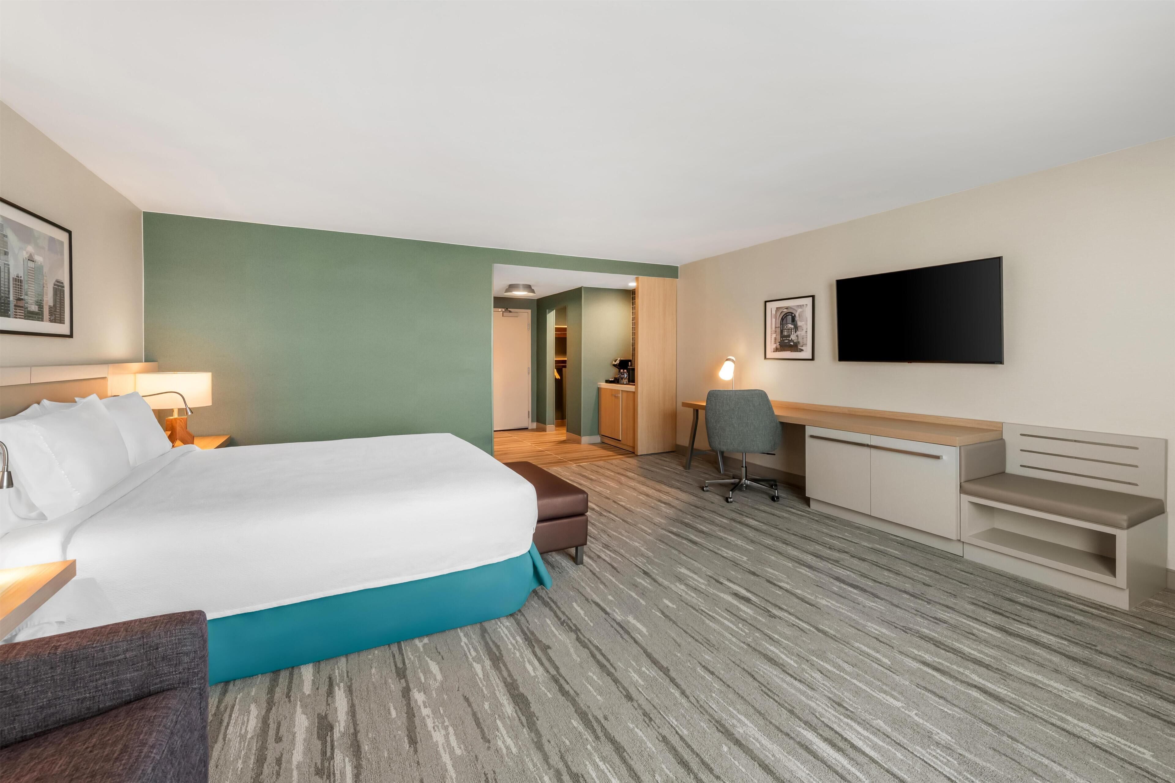 Una camera d'albergo con un letto, una scrivania, una sedia e una TV appesa al muro.