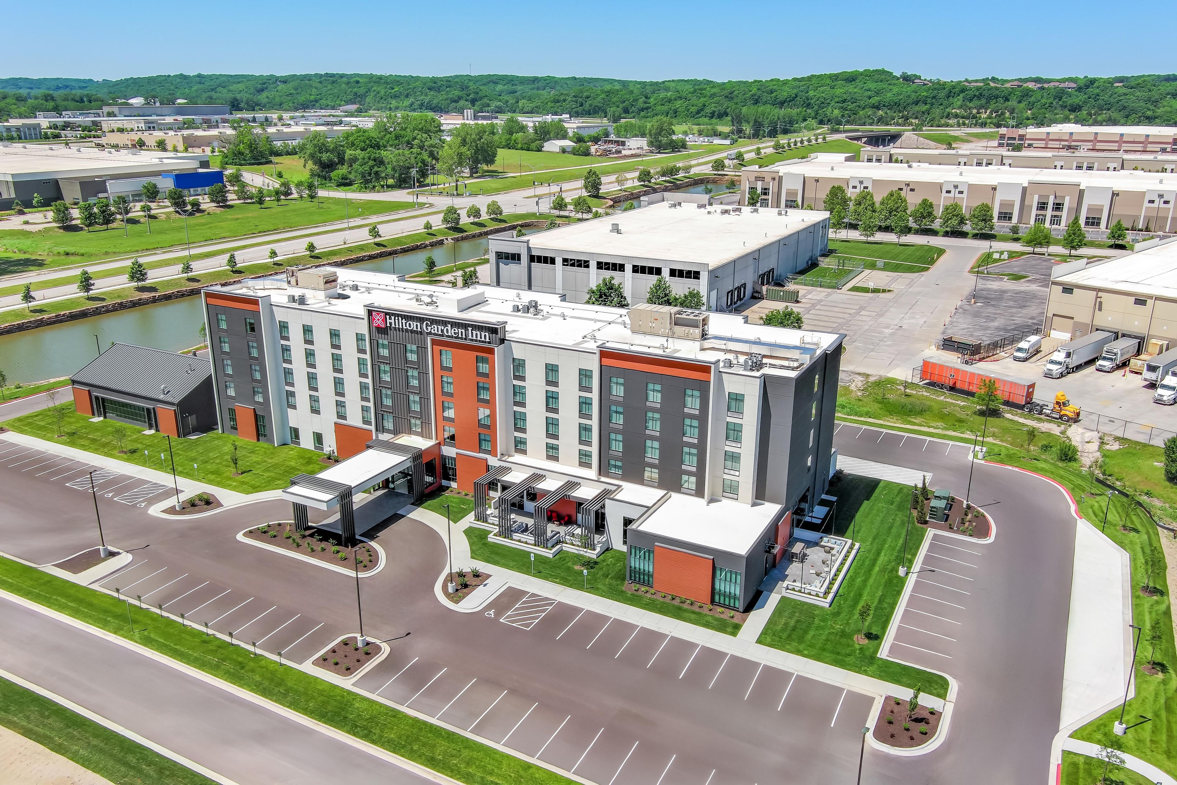Un hotel moderno con un letrero llamativo de Hilton Garden Inn, rodeado de un estacionamiento y un río.