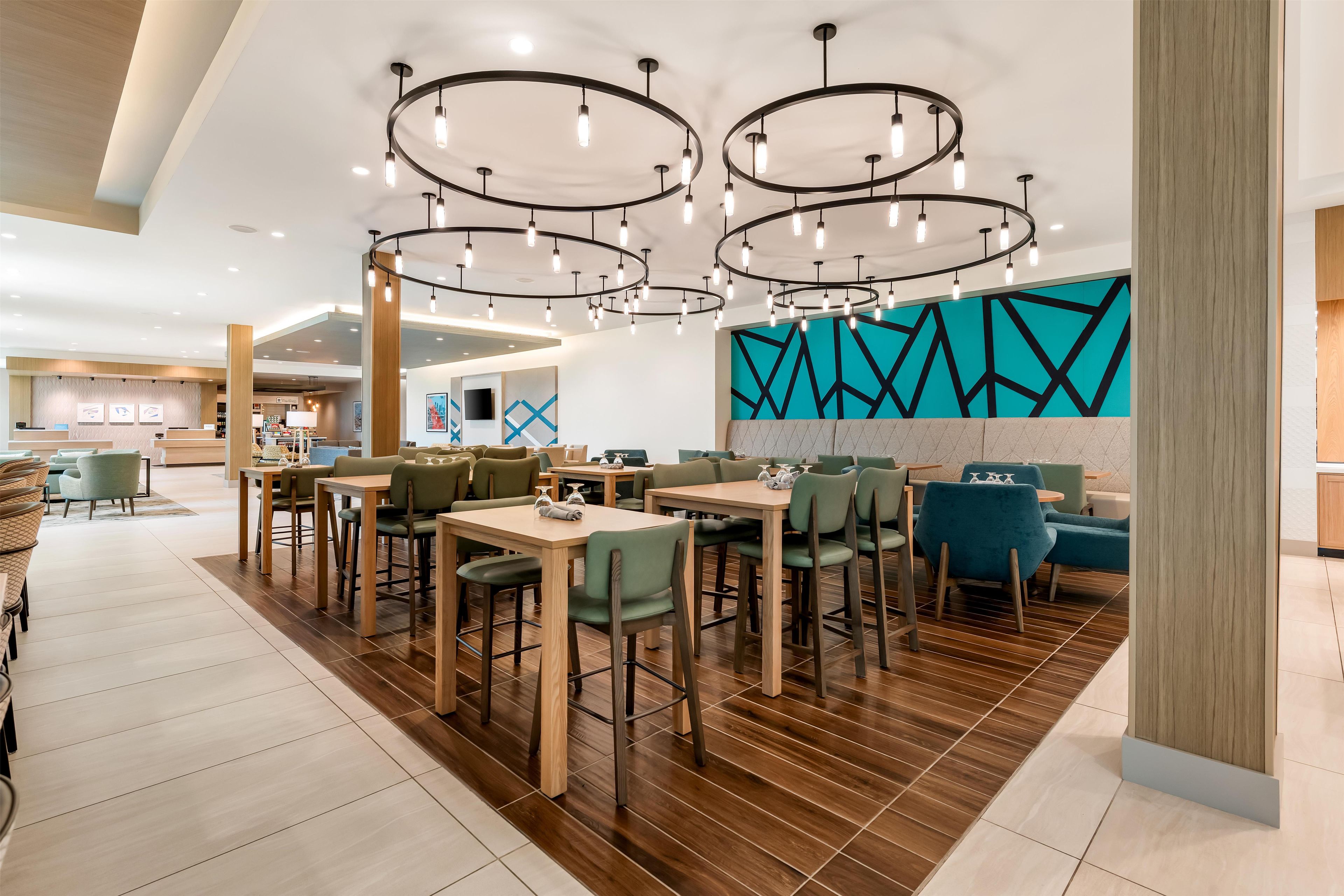 Un interno ristorante moderno con diversi tavoli e sedie, un lampadario centrale e un design geometrico della parete.
