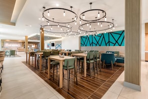 Interior de un restaurante moderno con varias mesas y sillas, una lámpara central y un diseño geométrico en la pared.