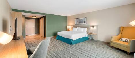 Une chambre d’hôtel avec un lit, un bureau, une chaise, un canapé et un tableau représentant un paysage urbain accroché au mur.