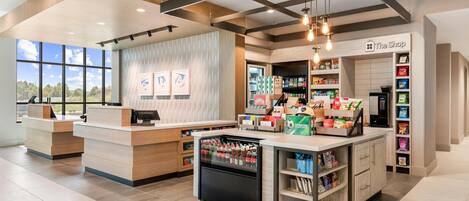 A modern retail store with a central counter, refrigerated display, and shelves stocked with snacks.