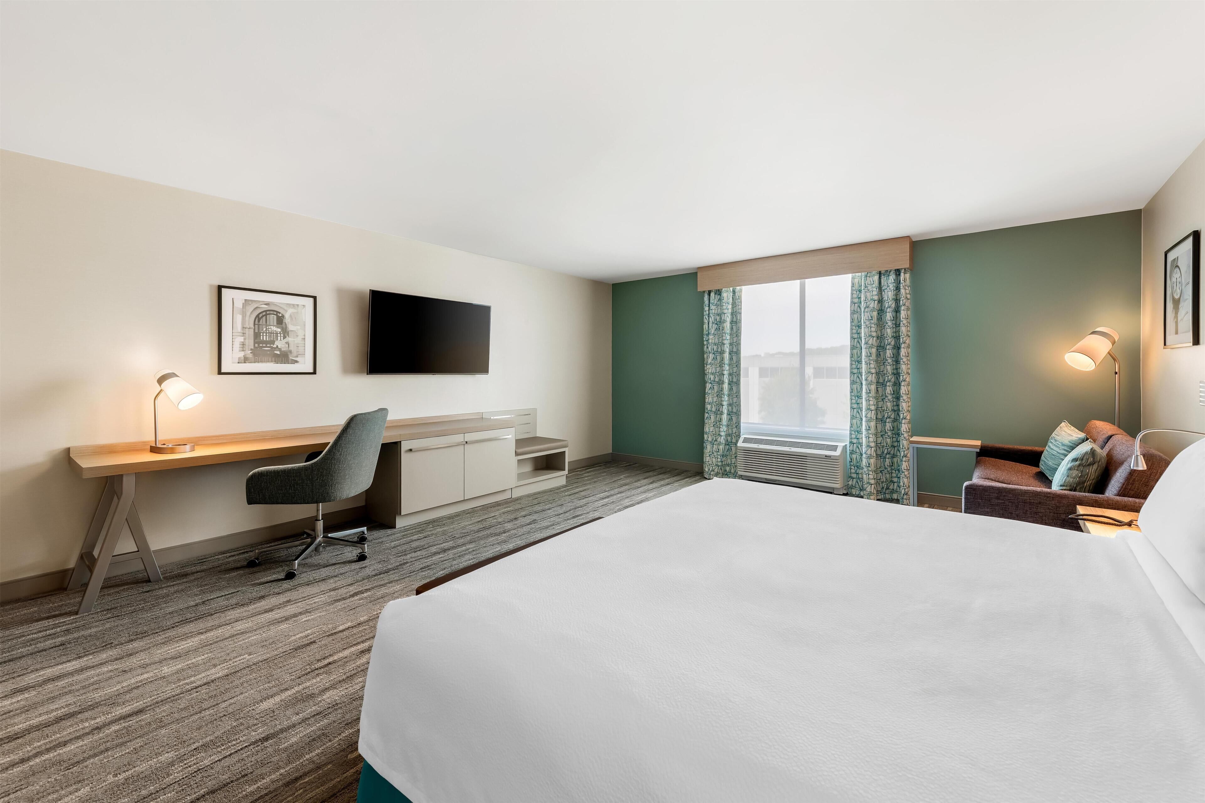A hotel room with a bed, a desk, a chair, a TV, and a window with curtains.