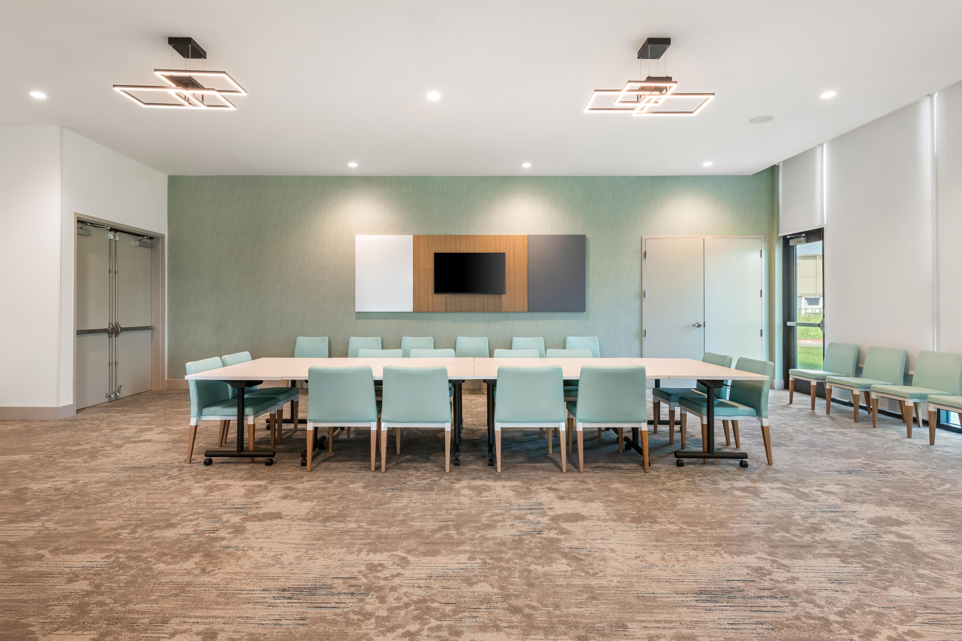 A conference room with a long table, chairs, a flat-screen TV, and recessed lighting.