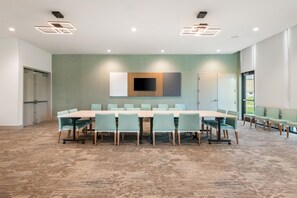 A conference room with a long table, chairs, a flat-screen TV, and recessed lighting. - Hilton Garden Inn Kansas City Riverside (Riverside)