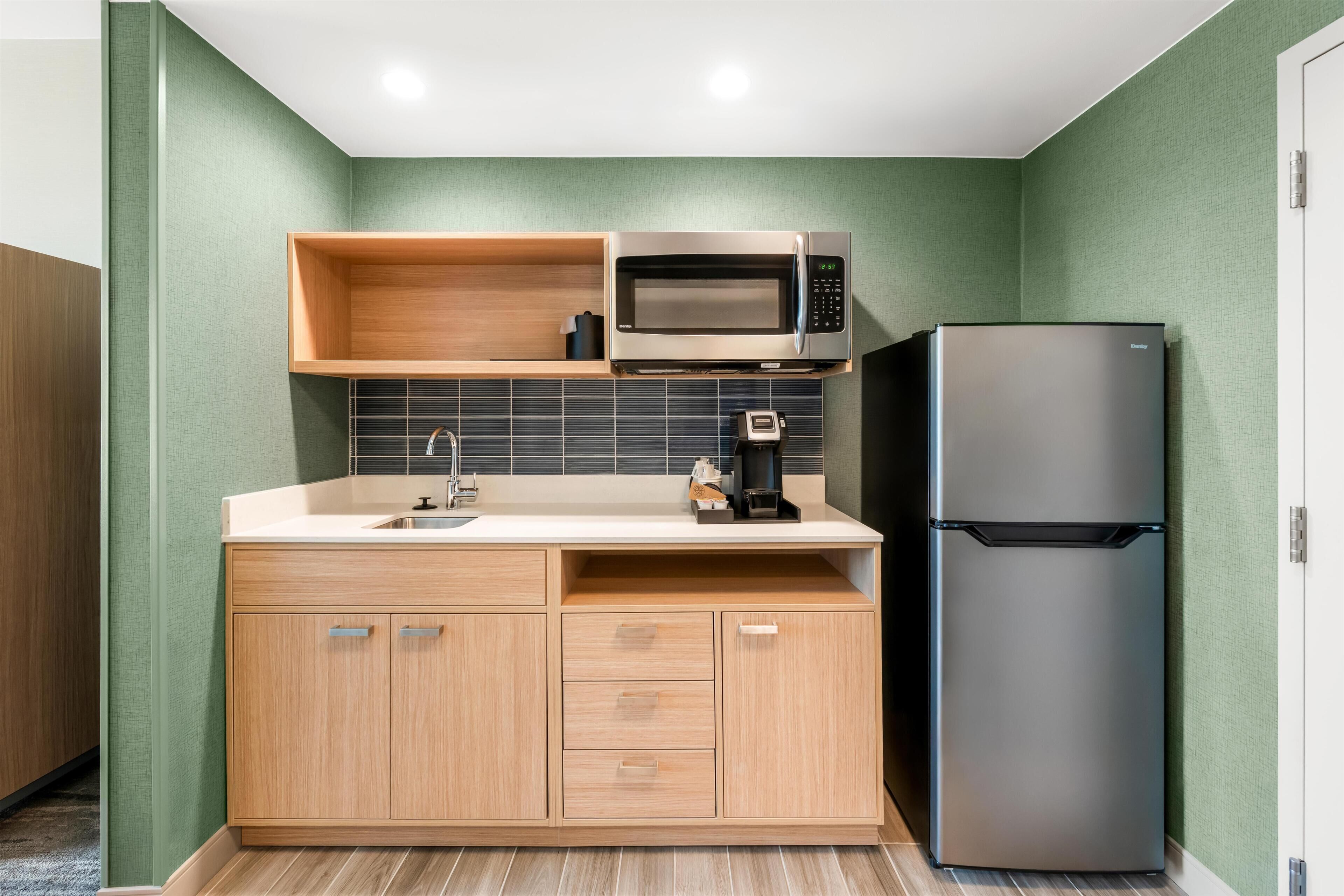 A compact kitchen with a built-in microwave, a stainless steel refrigerator, and wooden cabinetry.