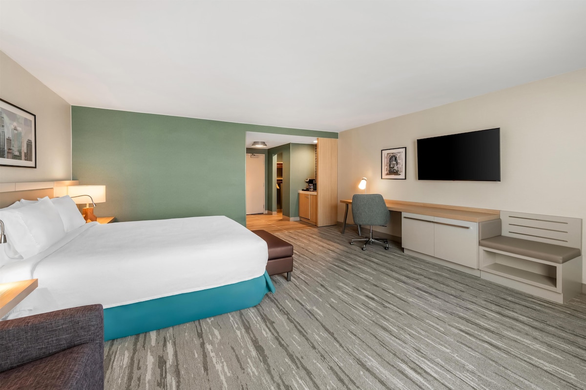 A hotel room with a bed, desk, chair, and a TV on the wall.