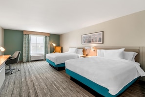 A hotel room with two beds, a desk, a chair, a window with curtains, a lamp, and a cityscape painting on the wall.