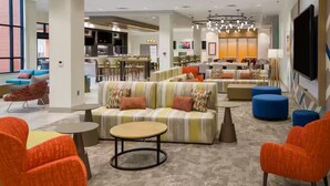 A modern hotel lobby with a sectional sofa, round tables, and colorful chairs. - Hilton Garden Inn Kansas City Riverside (Riverside)