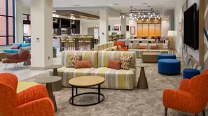 A modern hotel lobby with a sectional sofa, round tables, and colorful chairs. - Hilton Garden Inn Kansas City Riverside (Riverside)