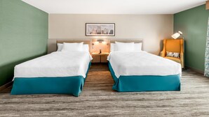 A hotel room with two beds, a nightstand, a lamp, and a framed cityscape picture on the wall. - Hilton Garden Inn Kansas City Riverside (Riverside)