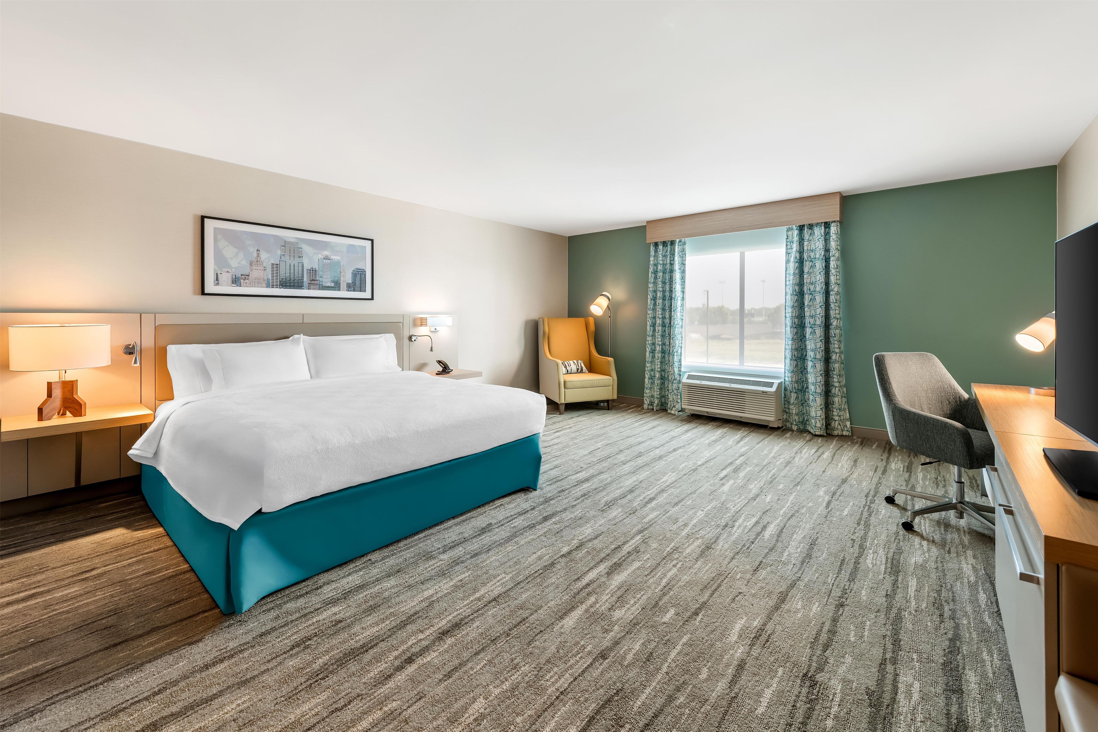 A hotel room with a bed, a desk, a chair, a television, and a window with curtains.
