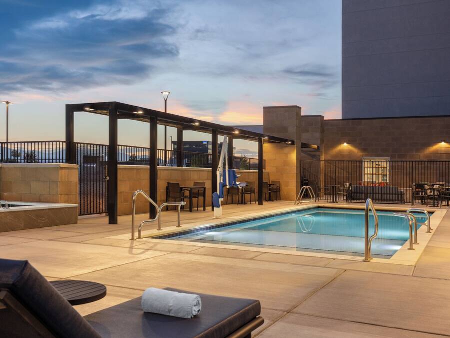Un área de piscina en la azotea con sillones de descanso, un espacio de estar techado y vistas a la ciudad.
