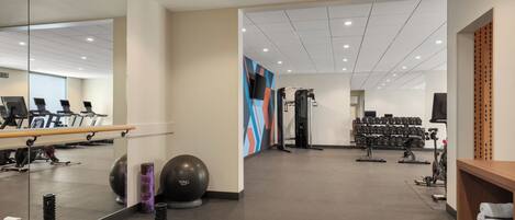 Ein Fitnessraum mit Trainingsgeräten, einer Spiegelwand und einem farbenfrohen Wanddesign.