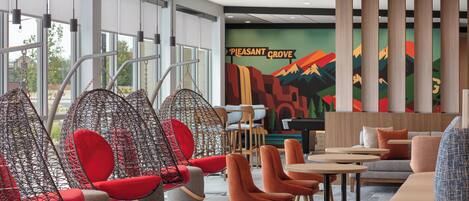 A modern lounge area with seating arrangements, including hanging chairs and sofas, and a colorful mural on the wall.