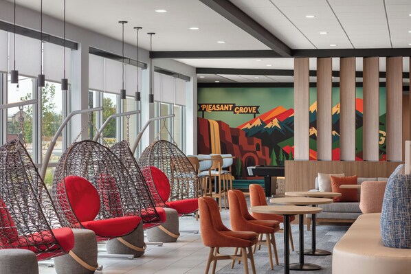 A modern lounge area with seating arrangements, including hanging chairs and sofas, and a colorful mural on the wall. - Tru By Hilton Pleasant Grove Provo North (Lindon)