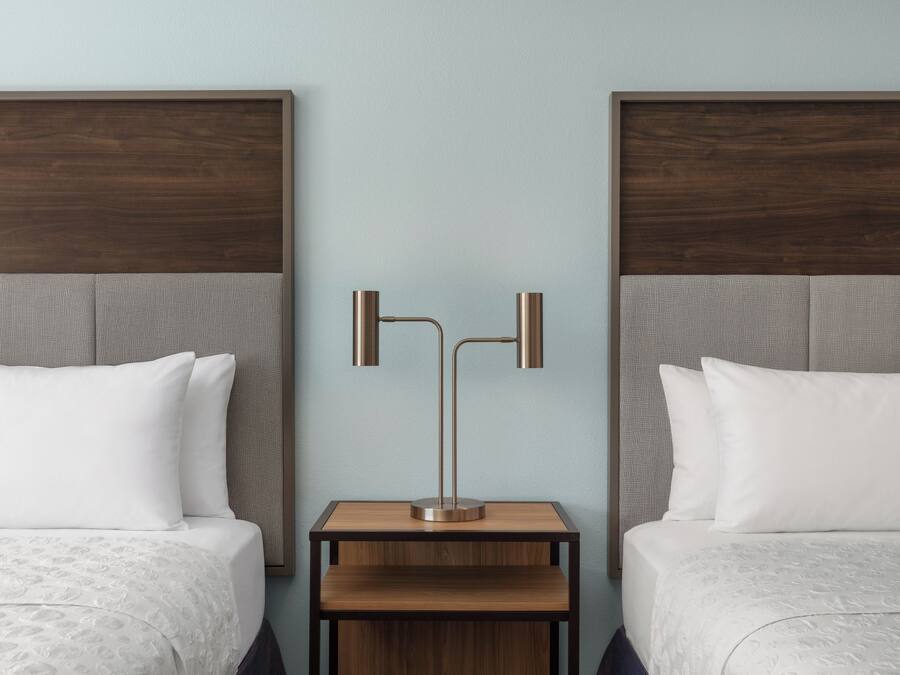 Una camera d'albergo con due letti, un comodino e una lampada a parete.