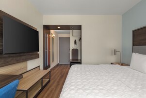 Habitación de hotel con cama, escritorio, televisor, armario y baño.