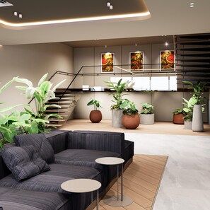 A modern interior with a sectional sofa, round tables, potted plants, a staircase, and artwork on the walls. - Hilton Garden Inn Pereira (Pereira)