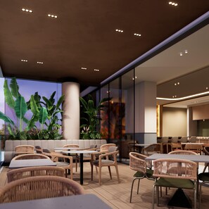 An indoor seating area with round tables and wicker chairs, surrounded by large windows and indoor plants. - Hilton Garden Inn Pereira (Pereira)