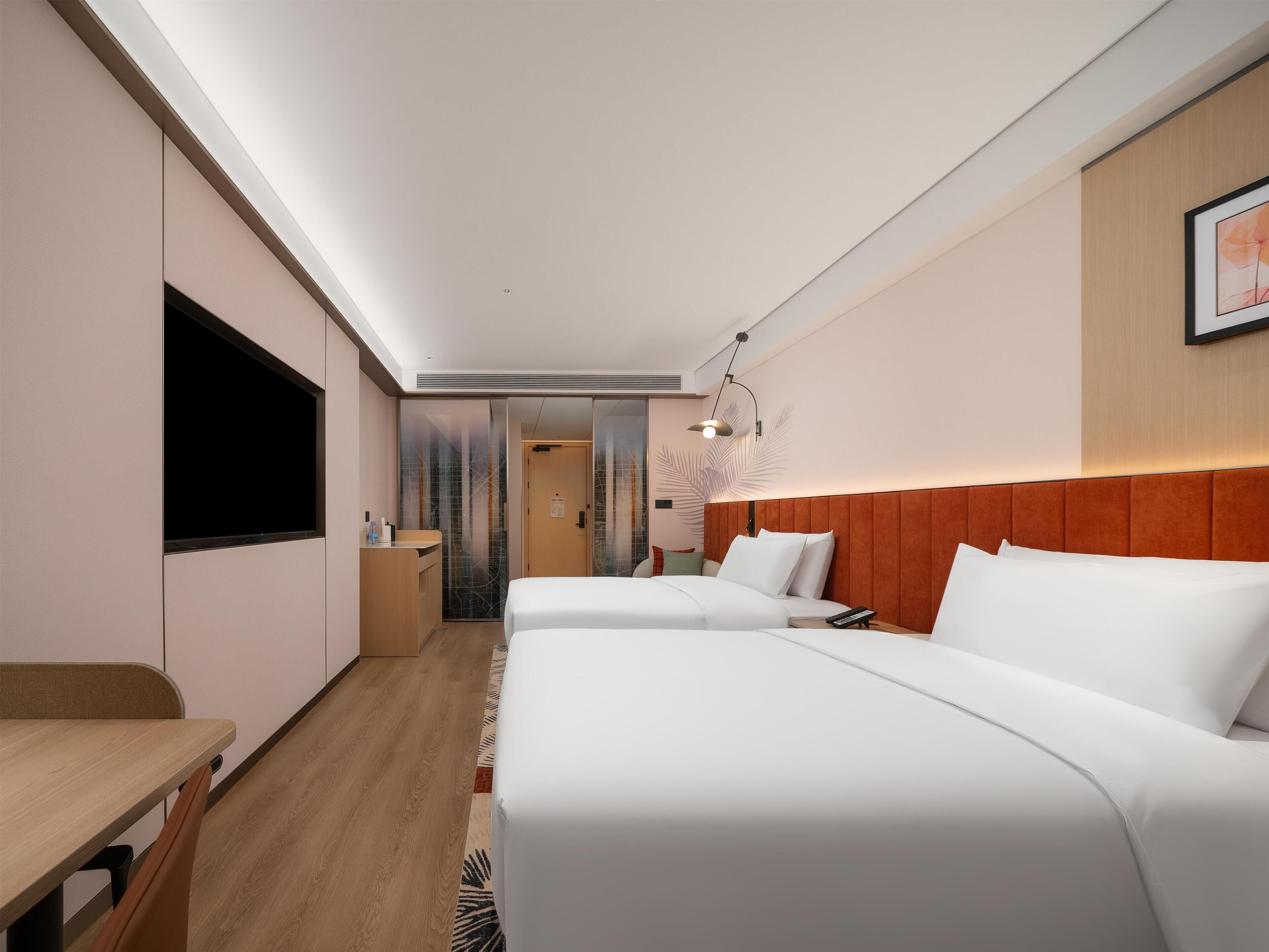 A hotel room with a large flat-screen TV, two beds, a wooden desk, and a shower area.