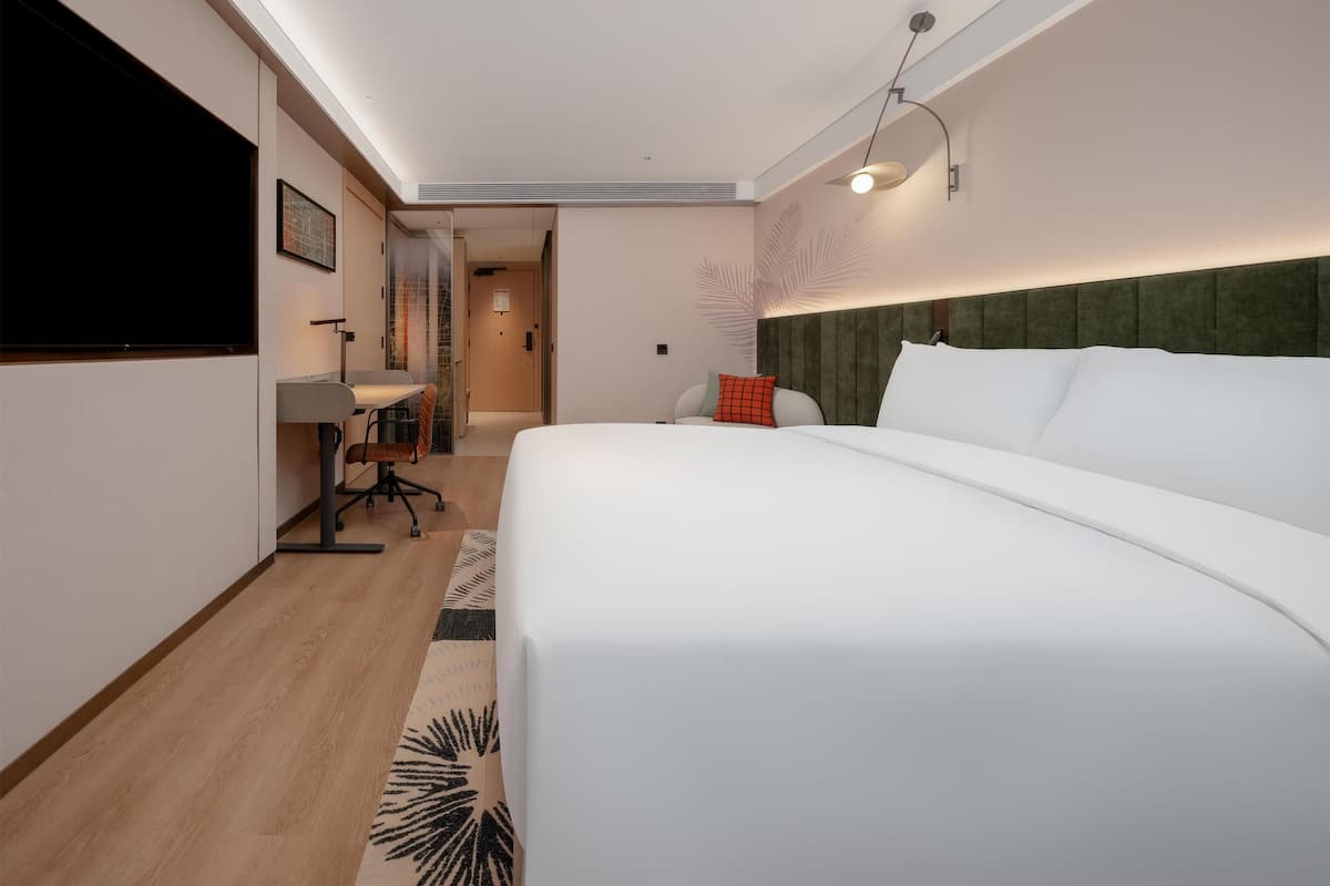 Una habitación de hotel con cama, escritorio, silla y televisor montado en la pared.
