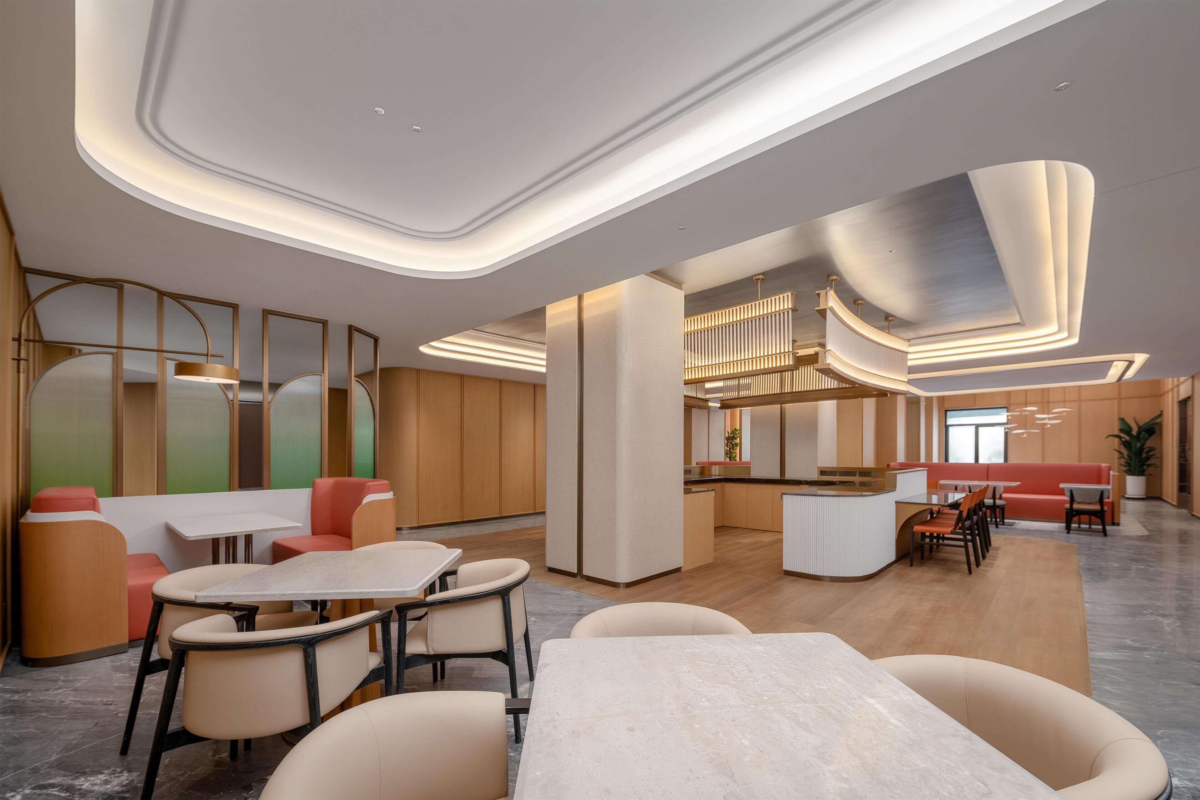 A modern hotel lobby with a central seating area, a kitchen, and a reception desk.
