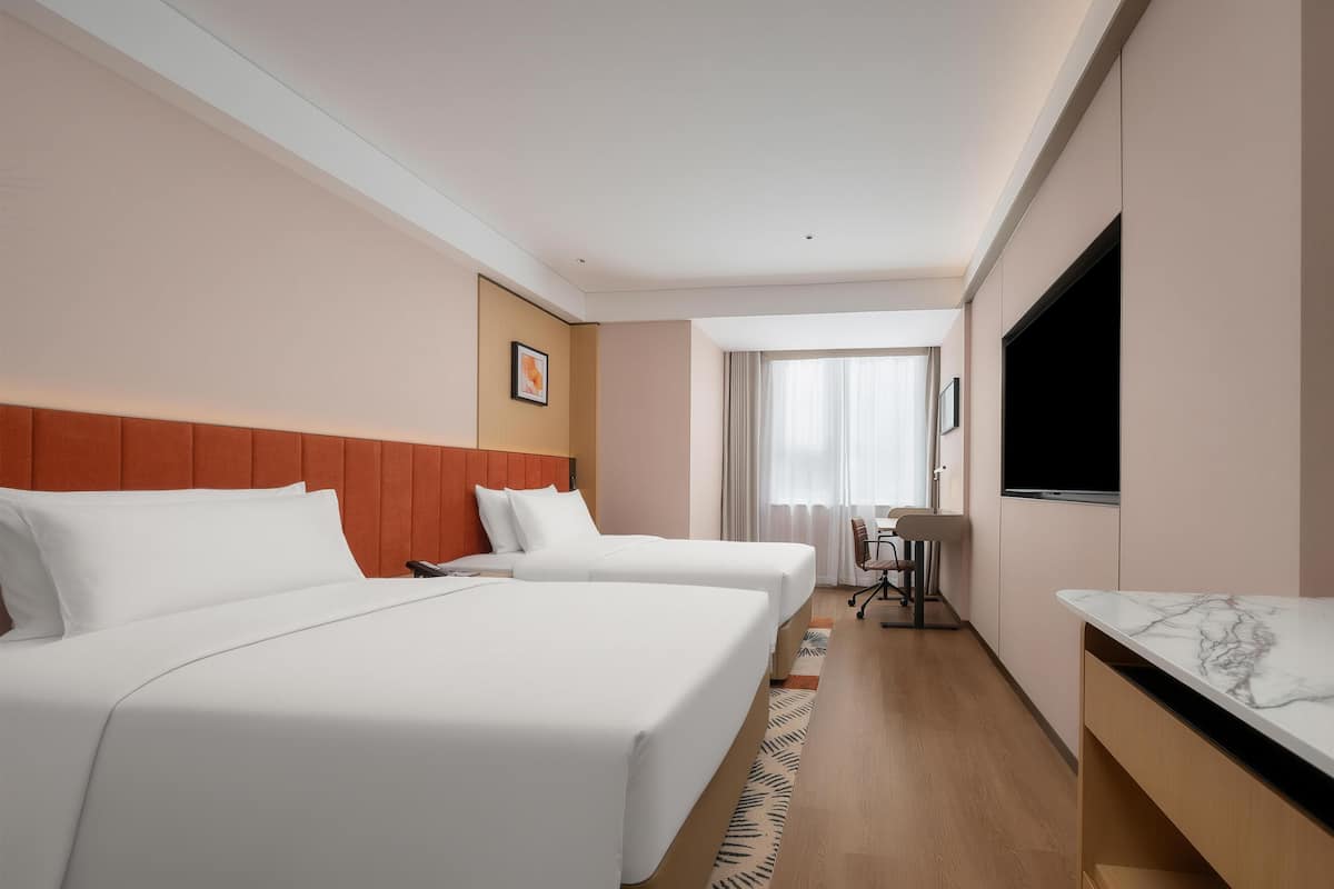 Habitación de hotel con dos camas, televisión, escritorio y ventana con cortinas.
