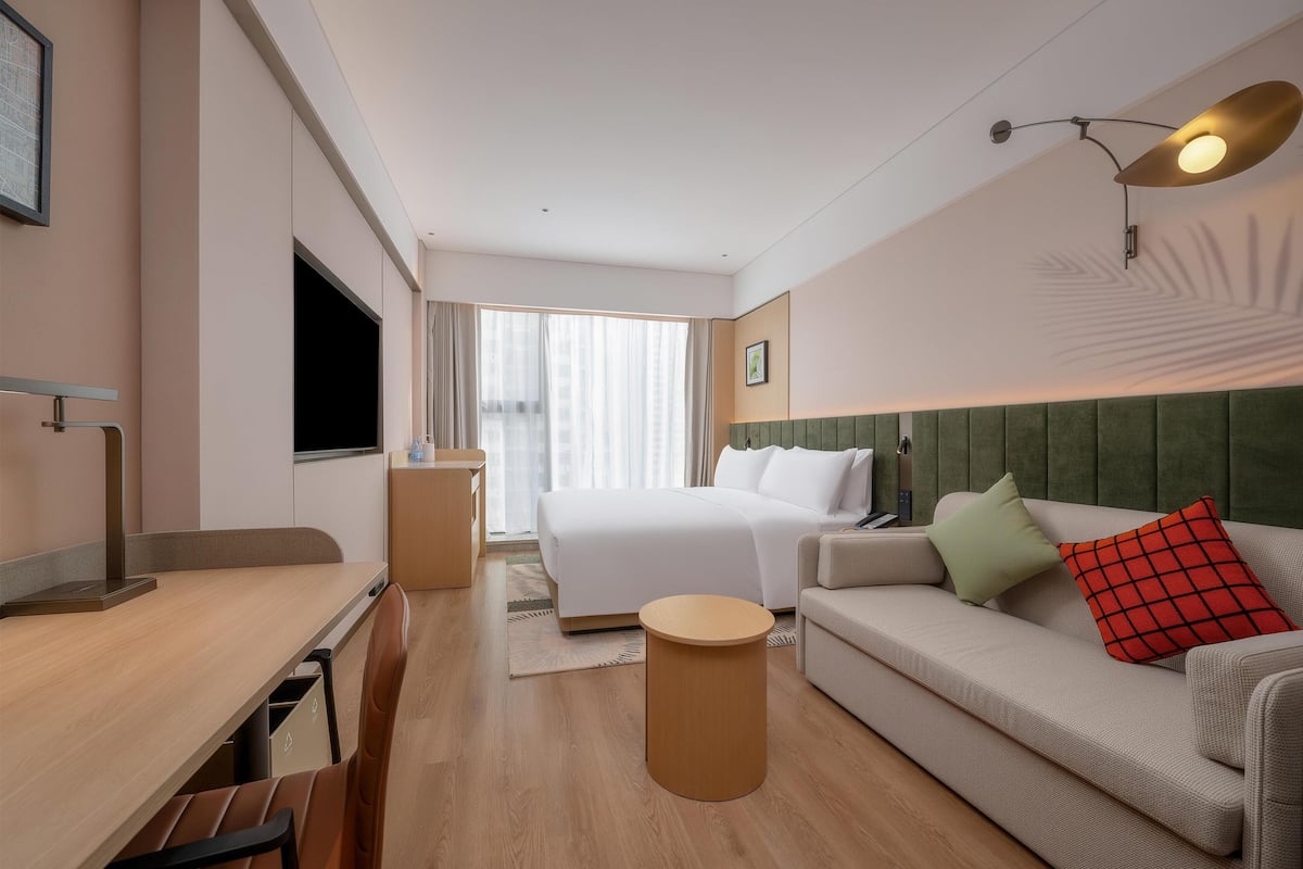 Habitación de hotel con cama, sofá, escritorio, silla, televisión y ventana con cortinas.