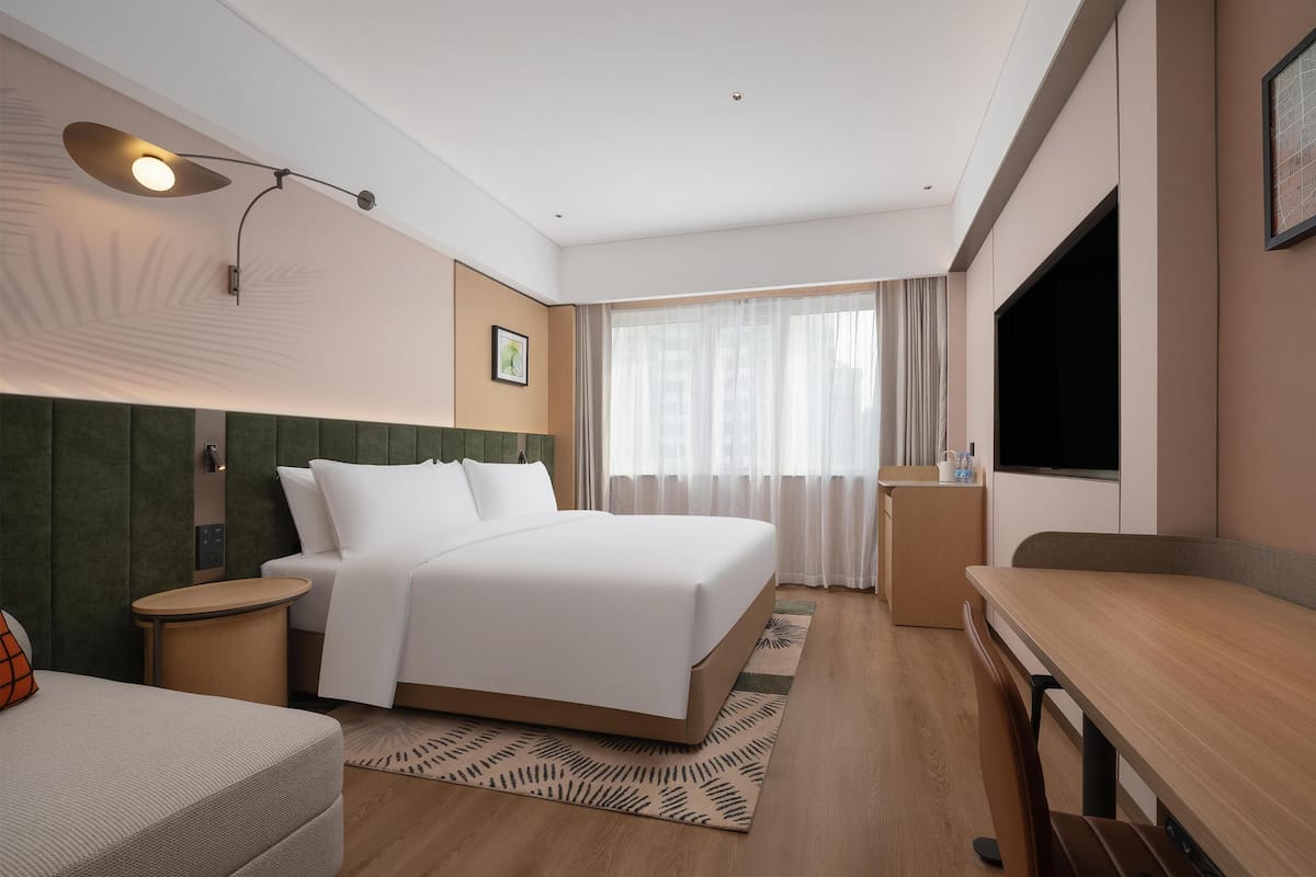 Habitación de hotel con cama, mesita de noche, escritorio, silla, televisión y ventana con cortinas.