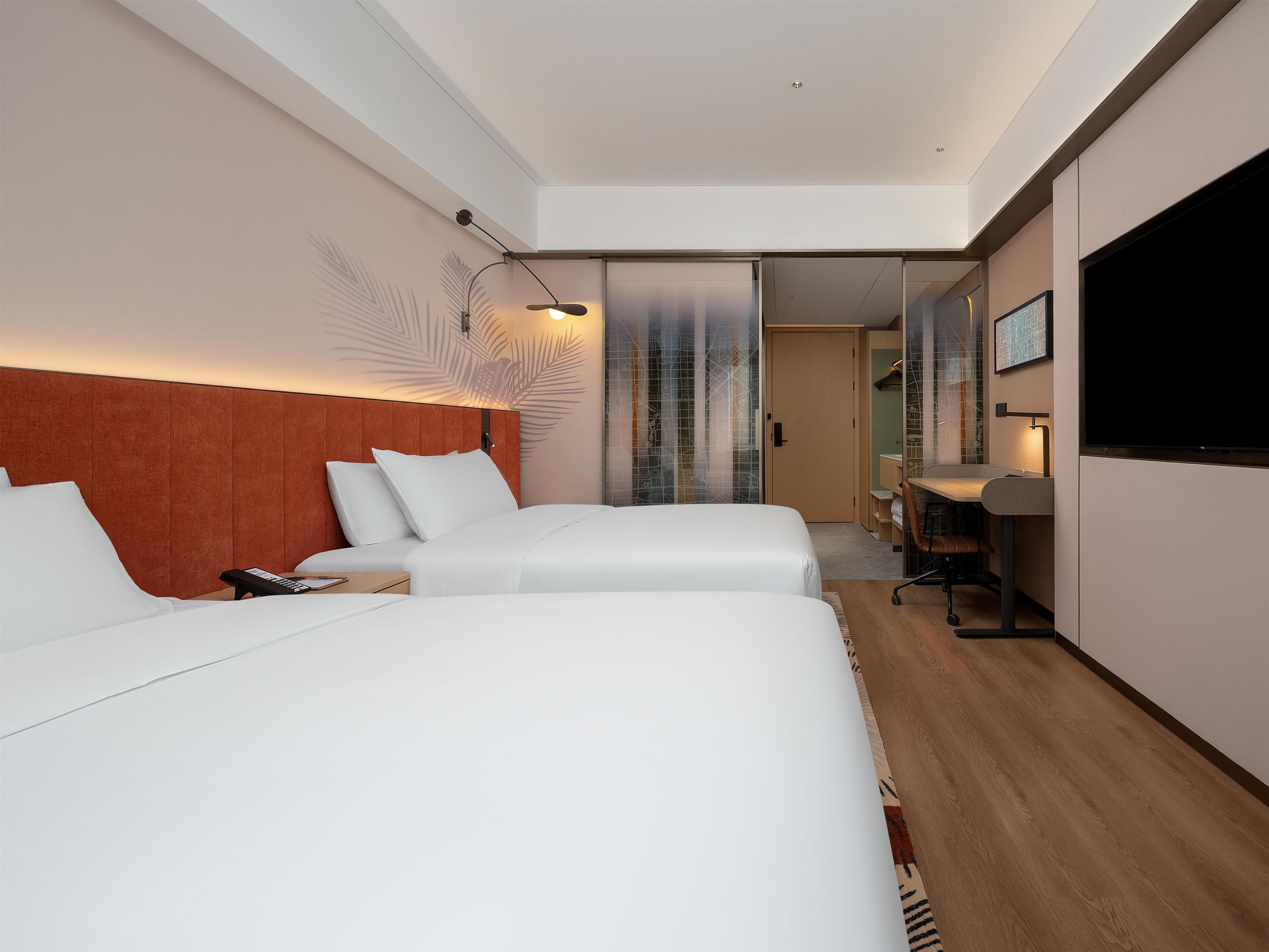 A hotel room with two beds, a desk, a TV, and a sliding door leading to a bathroom.