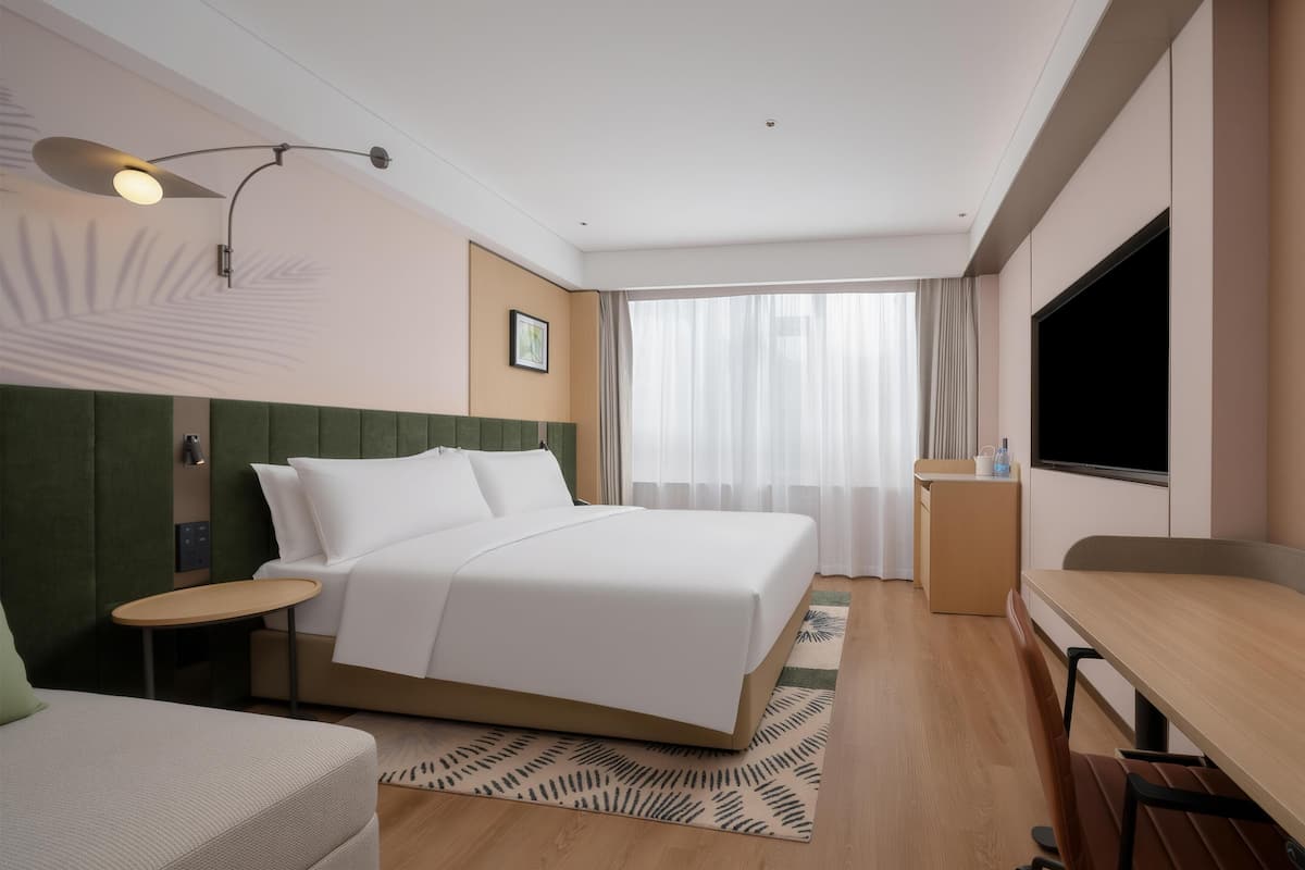 Habitación de hotel con cama, mesita de noche, lámpara, televisor y un pequeño escritorio con silla.