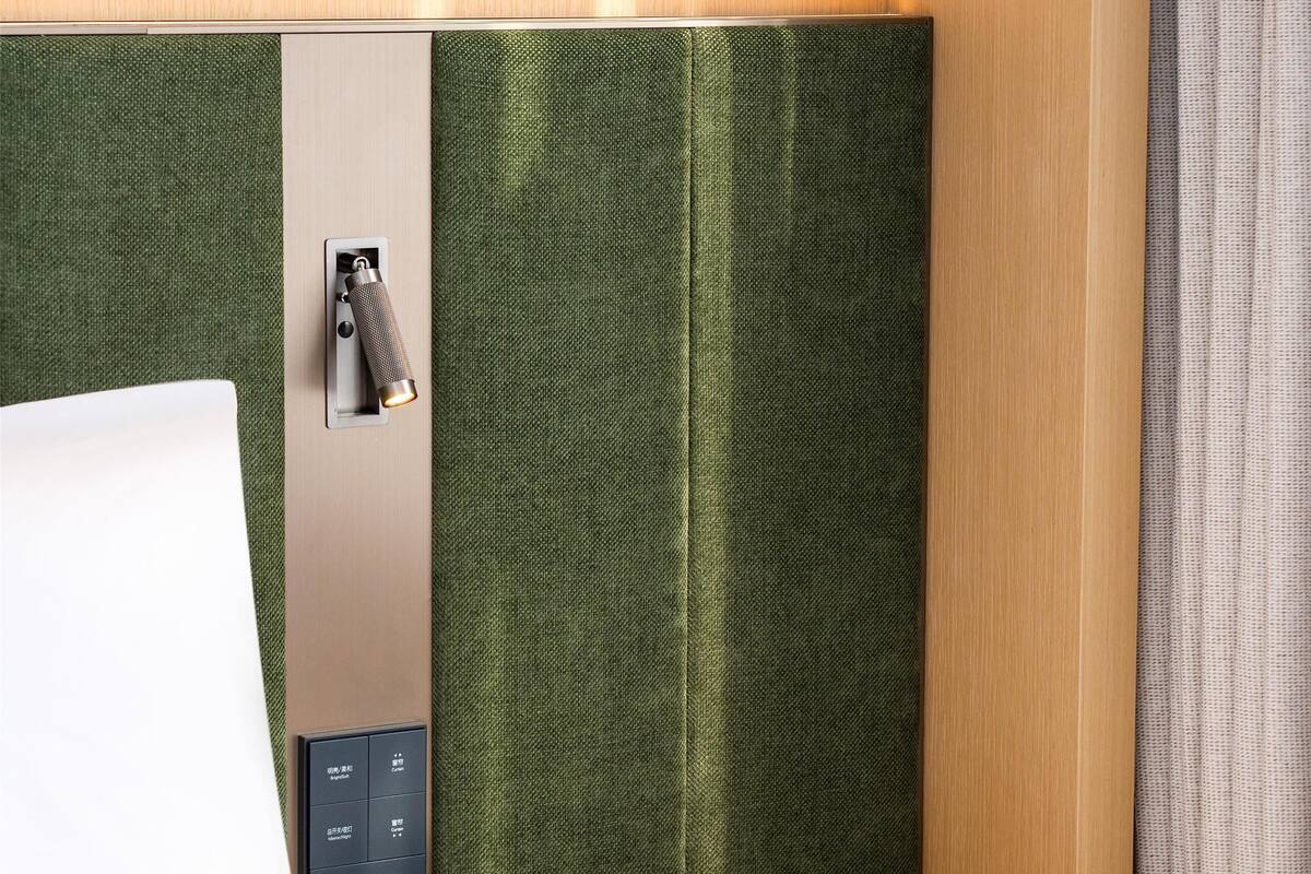 Habitación de hotel con un escritorio de madera, un teléfono, una libreta y una lámpara fijada a la pared.