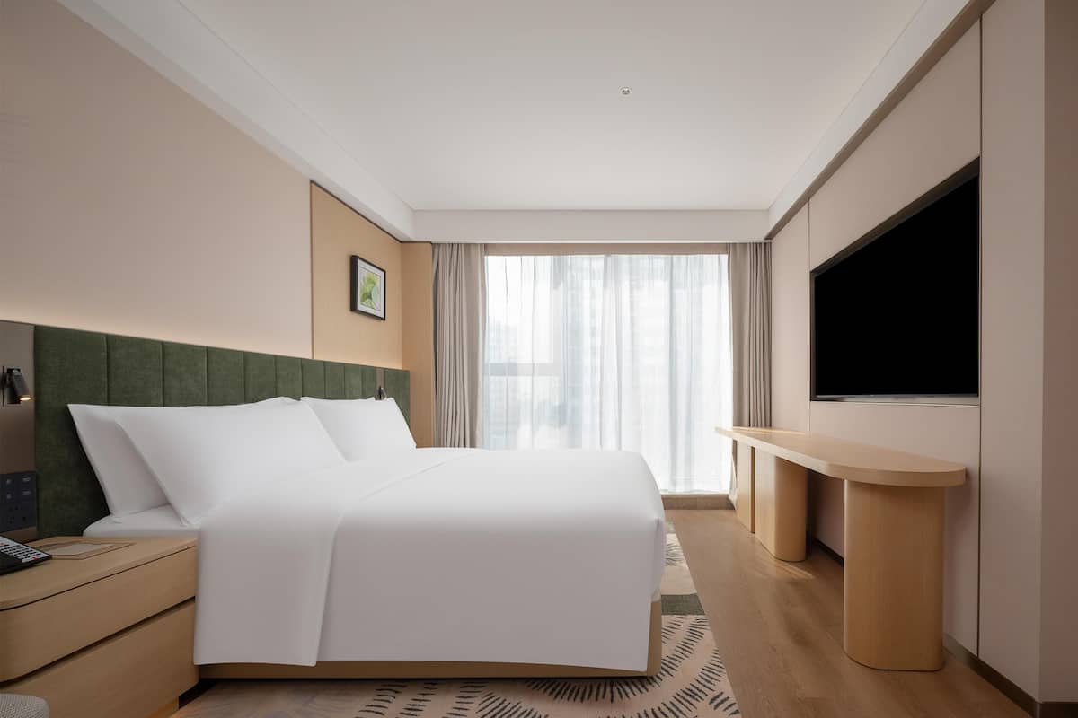Una habitación de hotel con cama, mesita de noche, televisor y ventana con cortinas.