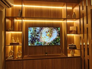 A wooden entertainment unit with a flat-screen TV, shelves with decorative items, and built-in lighting. - Beachfront Apartment in Ondina Near Carnival 2 (Salvador)