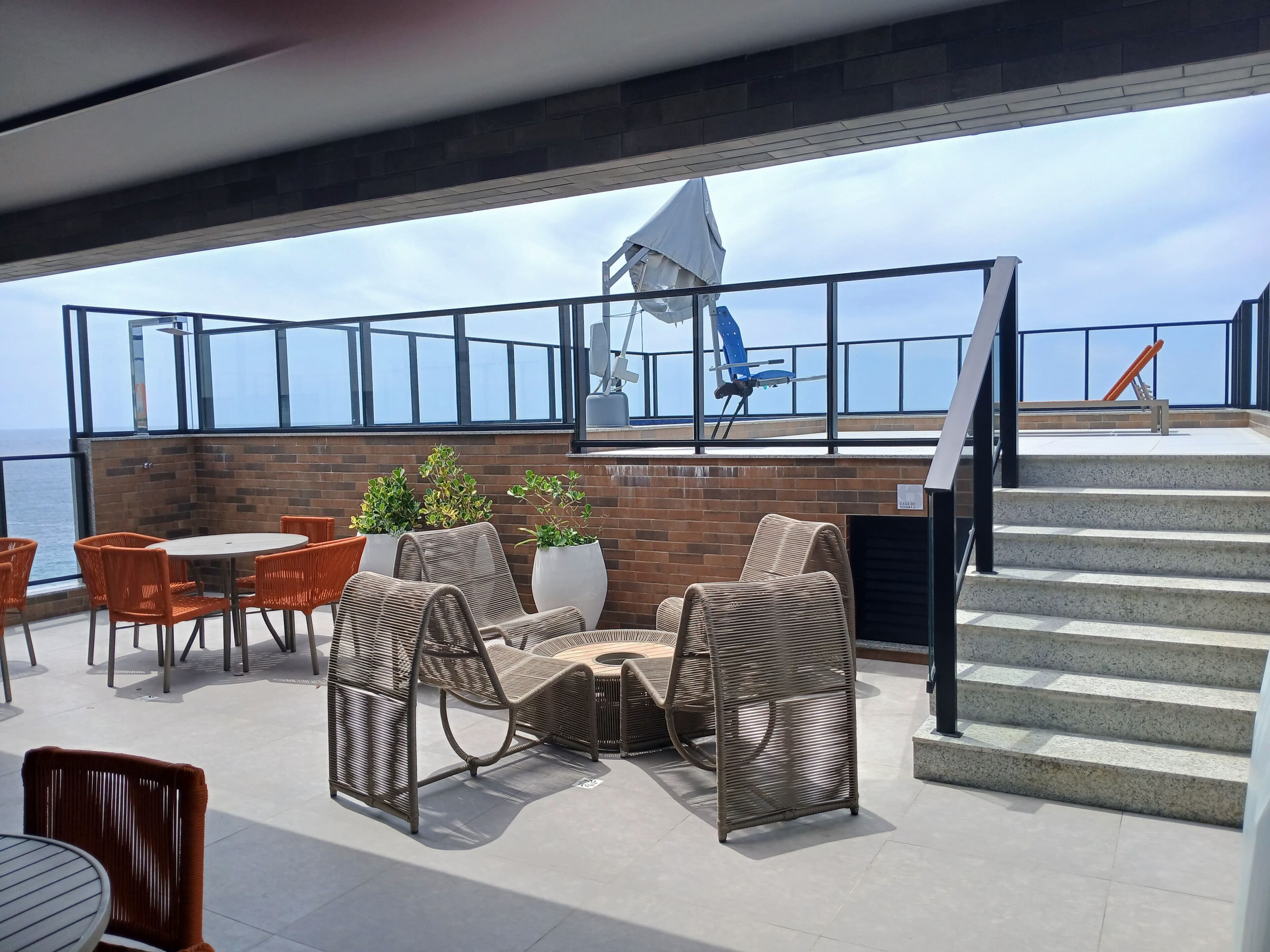 A rooftop terrace with wicker furniture, a table, potted plants, and a view of the sea.