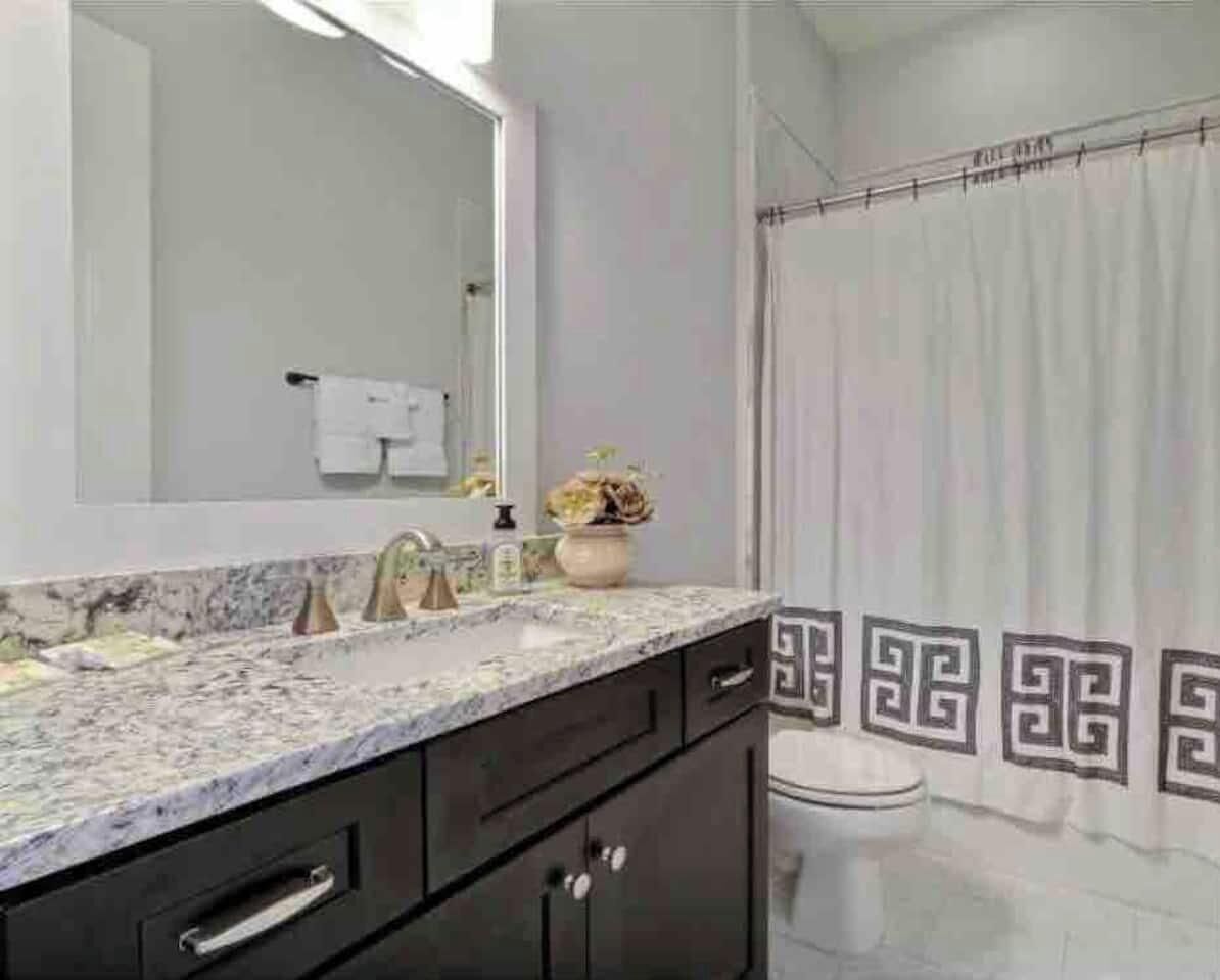 A bathroom with a marble countertop, a sink, a mirror, a toilet, and a shower curtain with a geometric pattern.