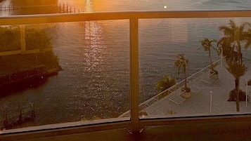 Vista del atardecer desde un balcón con vista a un cuerpo de agua, un puente y edificios a lo lejos.