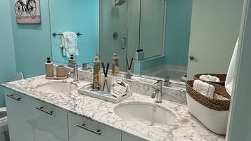 A modern bathroom with a large mirror, two sinks, and a shower.