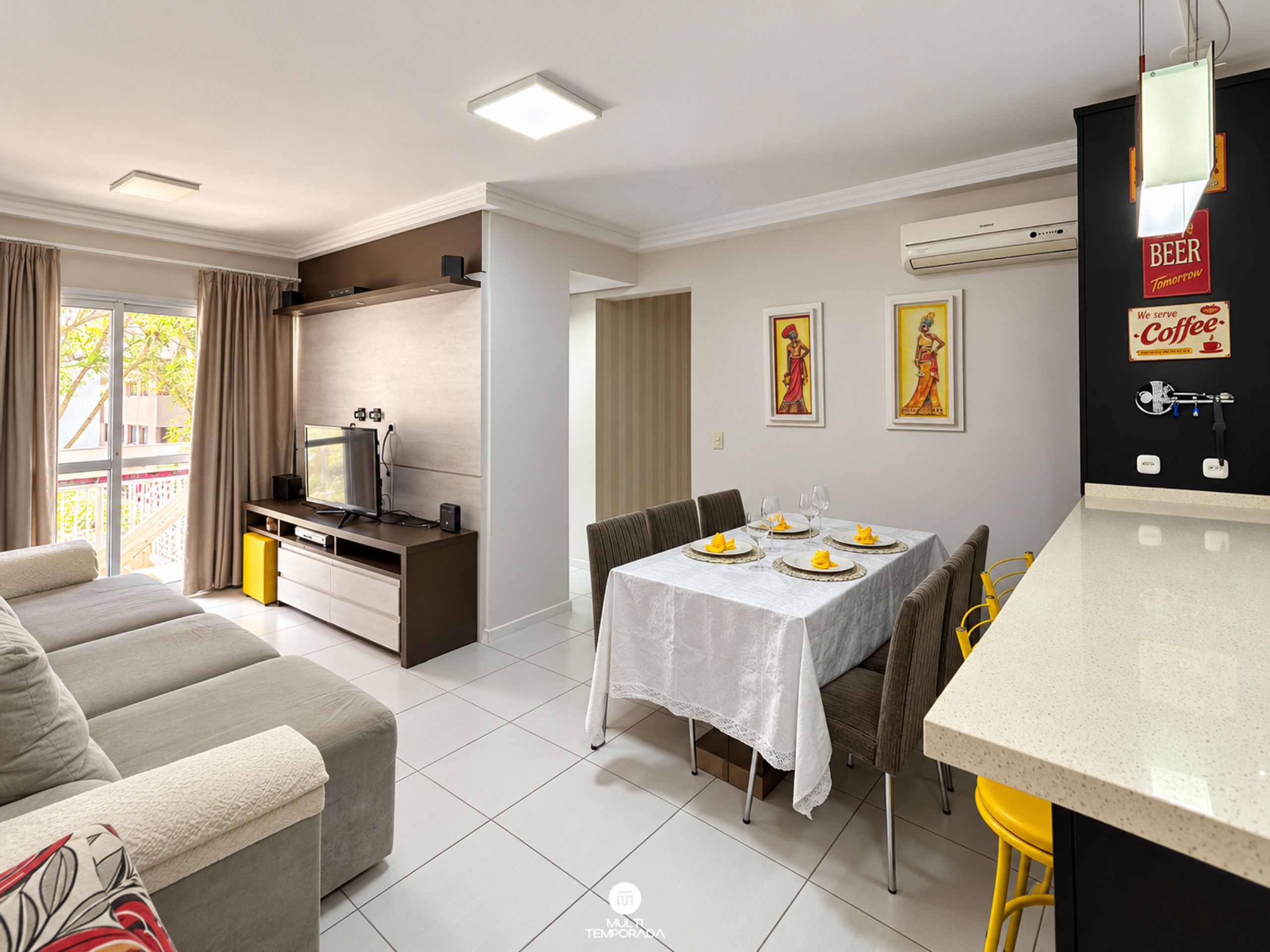 Un salon moderne avec un canapé, un coin repas avec une table dressée pour deux personnes et un espace cuisine doté d’un comptoir et d’une machine à café.