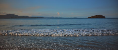 A beach with waves, a distant island, and mountains.