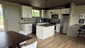 A modern kitchen with white cabinetry, a central island, stainless steel appliances, and a dining area with a wooden table and chairs.