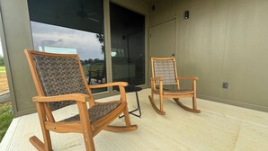 Two rocking chairs on a wooden deck with a glass door leading to a covered area.