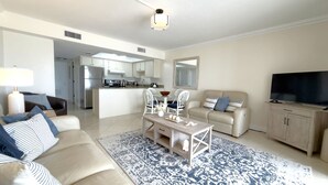 A living room with a sofa, coffee table, TV, and a kitchen in the background. - Gateway Villas #295 “Coastal Villa Reatreat” (Fort Myers Beach)