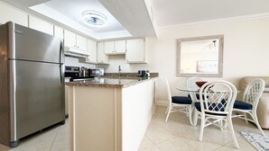 A compact kitchen with a refrigerator, microwave, stove, and a dining area with chairs and a table. - Gateway Villas #295 “Coastal Villa Reatreat” (Fort Myers Beach)